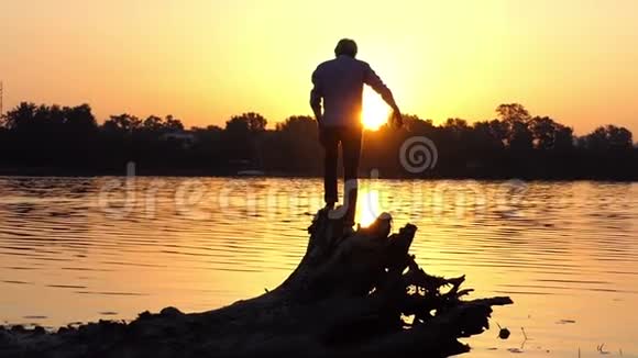 年轻人站在邋遢的湖岸上的树根上视频的预览图