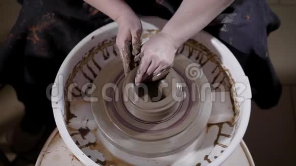 熟练的工匠坐在陶艺创作车间俯视图正在塑造和校正车轮头上的泥杯视频的预览图