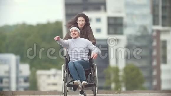 坐在轮椅上的快乐残疾人和在城市大街上奔跑的快乐年轻女子视频的预览图