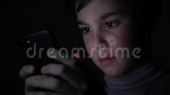 快乐男孩在家里的黑暗中玩着智能手机孩子的脸被一道亮光照亮视频的预览图
