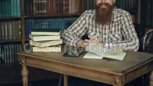一个年轻的大胡子男人在图书馆里微笑着看着镜头视频的预览图