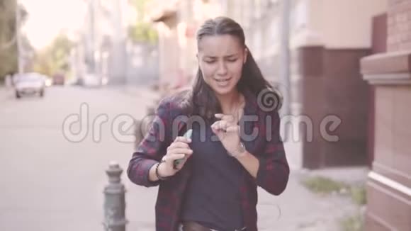 美丽的年轻开朗的女孩正在城里散步跑着摆手听耳机音乐视频的预览图