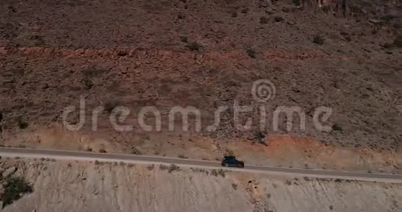 在山路上行驶的黑色汽车的鸟瞰图无人驾驶飞机飞过碎石路视频的预览图