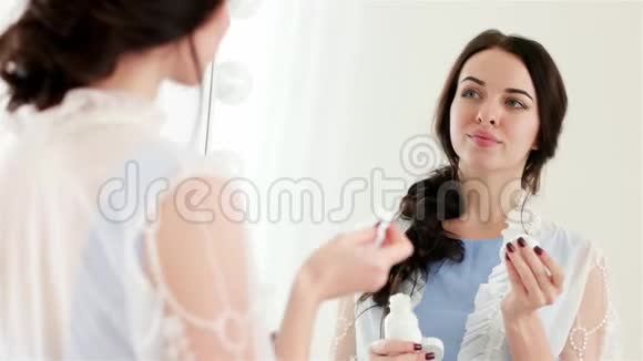 在镜子前用棉签清洁面部迷人的女人涂上洁肤补品视频的预览图