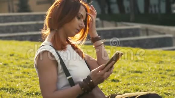 戴着红色头发的女人拿着手机在夏季公园视频的预览图