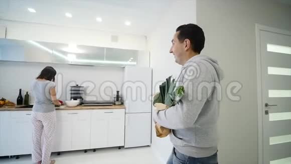 一个在厨房做饭的女人和她丈夫带来的产品视频的预览图
