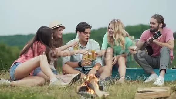 快乐的朋友喝啤酒开心地坐在篝火旁视频的预览图