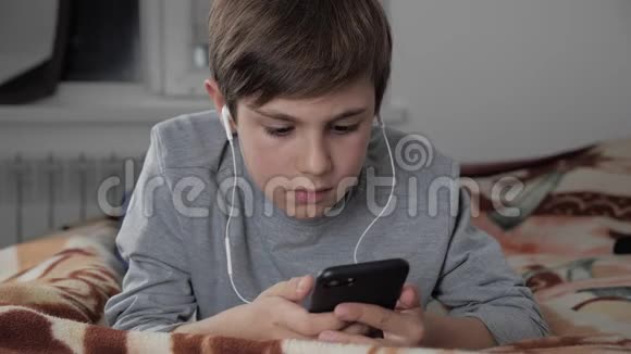 小孩玩手机带耳机在家小孩躺在床上使用智能手机视频的预览图