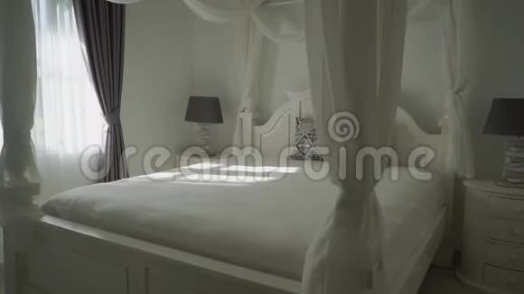 在一间小设计的卧室里有一张白色大床室内白色床头柜上有两盏灯窗户上有窗帘视频的预览图