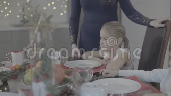 爱的母亲亲吻小可爱的女儿坐在餐桌上在舒适可爱的节日气氛中庆祝圣诞节视频的预览图