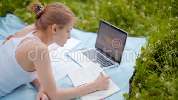好女孩正在公园里学习夏天在草地上用笔记本电脑和笔记本视频的预览图