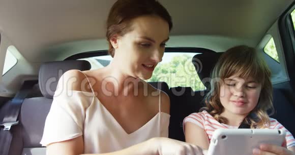 母亲和女儿在汽车后座使用数字平板电脑视频的预览图