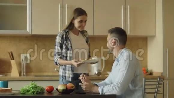 厨房里的漂亮情侣当他的女朋友在喂他时他正在玩平板电脑视频的预览图