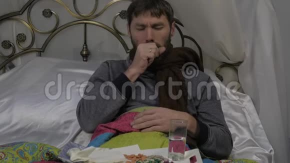 一个病人躺在床上脖子上围着一条温暖的围巾咳嗽着喝着一片药丸慢动作视频的预览图