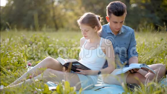 在夏日的阳光野餐中年轻美丽的情侣在户外看书视频的预览图
