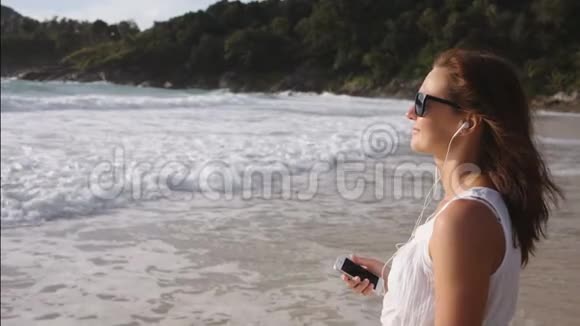 美丽的女人带着耳机在海滩上听音乐视频的预览图