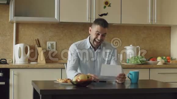 帅哥慢动作在家吃早餐时在厨房里听到好消息读信视频的预览图