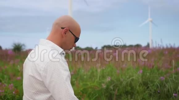 人类走过田野在风力涡轮机能源生产的背景下歌唱中弹视频的预览图