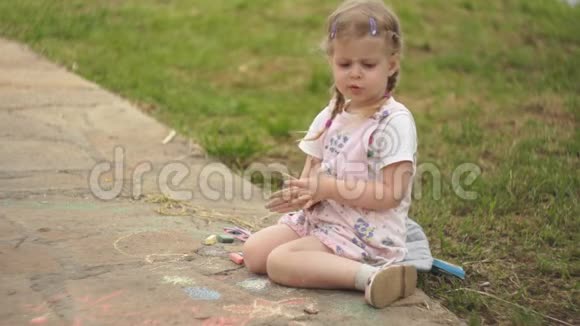 一个漂亮的小女孩在草地旁边的人行道上画粉笔视频的预览图