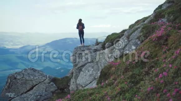 年轻女子穿着休闲装背着背包站在高高的山崖边上环顾四周视频的预览图
