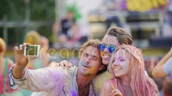 在彩色音乐节上年轻人微笑着在智能手机上摆姿势自拍视频的预览图