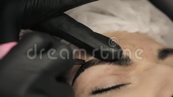特写美容师用黑色橡胶的手在眉毛上涂上永久的化妆眉毛纹身视频的预览图