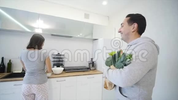 一个在厨房做饭的女人和她丈夫带来的产品视频的预览图