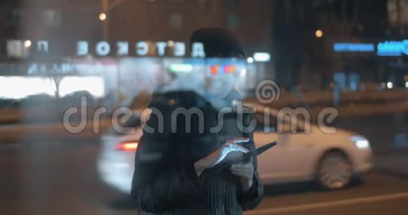 年轻女子在晚上的城市等公共汽车时在网垫上上网视频的预览图
