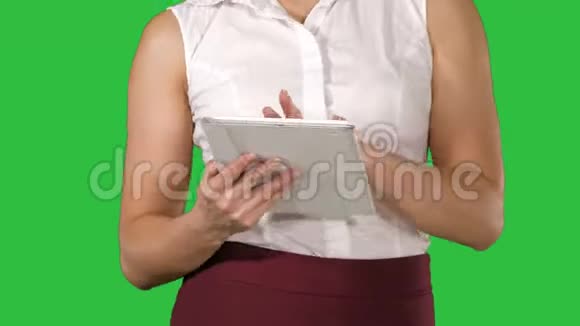 女人拿着数字平板电脑在绿色屏幕上行走时使用它Chroma键视频的预览图