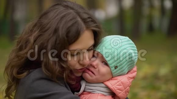 一幅美丽的年轻女子和一个哭泣的孩子在秋天公园的肖像小女孩在哭年轻的母亲安慰她视频的预览图