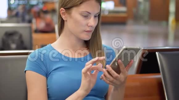 在机场候机楼等着的女人使用智能手机浏览与朋友聊天阅读新闻视频的预览图
