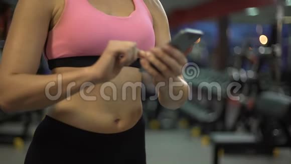 年轻女性在健身房手机上滚动设置培训应用程序视频的预览图