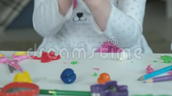 一个小女孩玩橡皮泥用手把它卷起来桌面上有数字和彩色铅笔视频的预览图