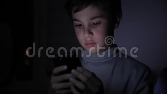 快乐男孩在家里的黑暗中玩着智能手机孩子的脸被一道亮光照亮视频的预览图
