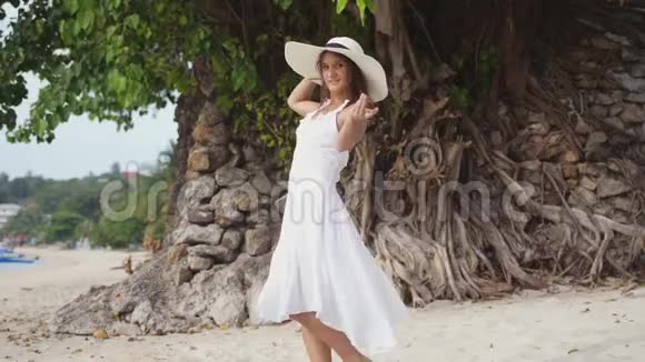 年轻的黑发女人长发戴着白色的衣服和帽子招手跟随她把帽子扔在热带海滩上慢慢慢慢视频的预览图