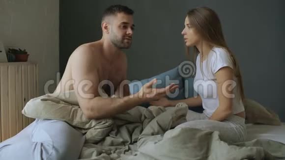 这对年轻夫妇坐在床上吵吵闹闹女人打她男朋友然后走开视频的预览图