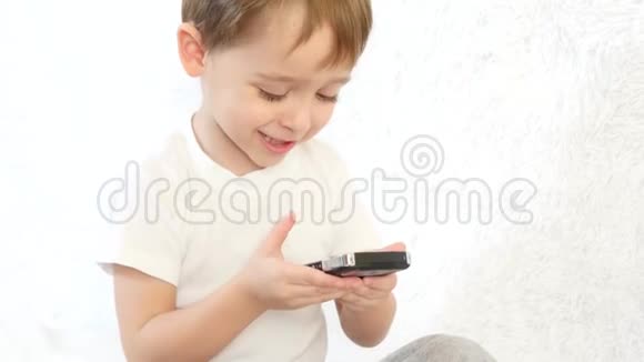 小男孩在白色背景上玩智能手机微笑着特写镜头视频的预览图