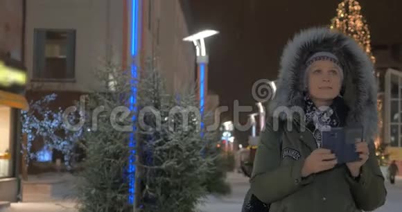 女人在街上用圣诞节的光照拍手机视频的预览图