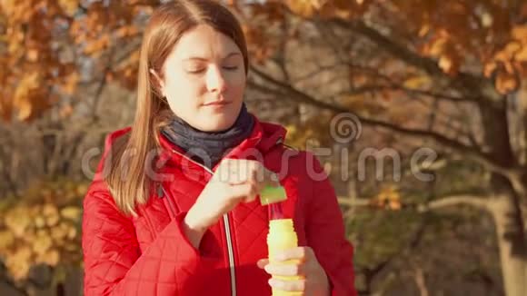 快乐的微笑女人享受大自然站在秋天的公园里穿着红色外套的女性制造肥皂泡视频的预览图