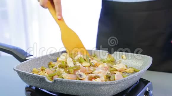 一个女人在煎锅里把木铲和鸡片和豆子和蘑菇混合在一起视频的预览图