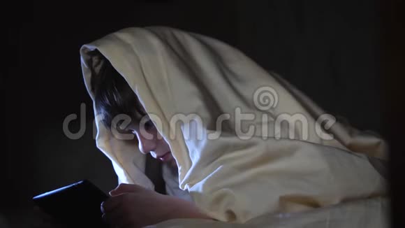 一个孩子晚上在毯子下面使用平板电脑这个男孩玩电脑游戏视频的预览图