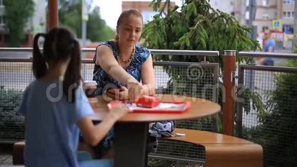 母亲和女儿正坐在一张桌子旁的一家街头咖啡馆里喝咖啡奶昔吃薯条视频的预览图