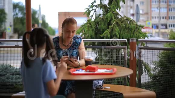 母亲和女儿正坐在一张桌子旁的一家街头咖啡馆里喝咖啡奶昔吃薯条视频的预览图