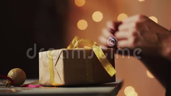 在圣诞灯光的背景下女人手把丝带绑在牛皮纸上背景视频的预览图