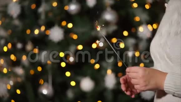 一名女子手中握着燃烧的孟加拉灯圣诞树后的近距离射击视频的预览图