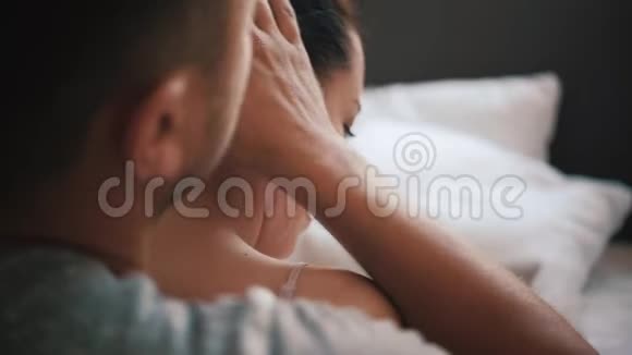 年轻快乐的一对恋人在家里的卧室里一起玩爱玩的妻子咬着微笑的丈夫的耳朵拥抱着视频的预览图
