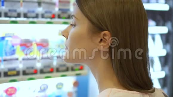 漂亮的饥饿女人从商场的自动售货机里挑选物品选择不健康的零食挨饿视频的预览图