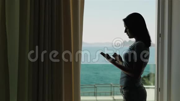 站在窗前使用平板电脑的年轻女性剪影视频的预览图