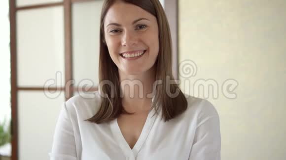 穿着白色上衣的年轻女子站在客厅微笑的双臂交叉着的慢镜头画像视频的预览图