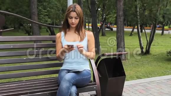 在城市公园的智能手机上聊天的女孩坐在公园里拿着小玩意的长凳上的女人视频的预览图